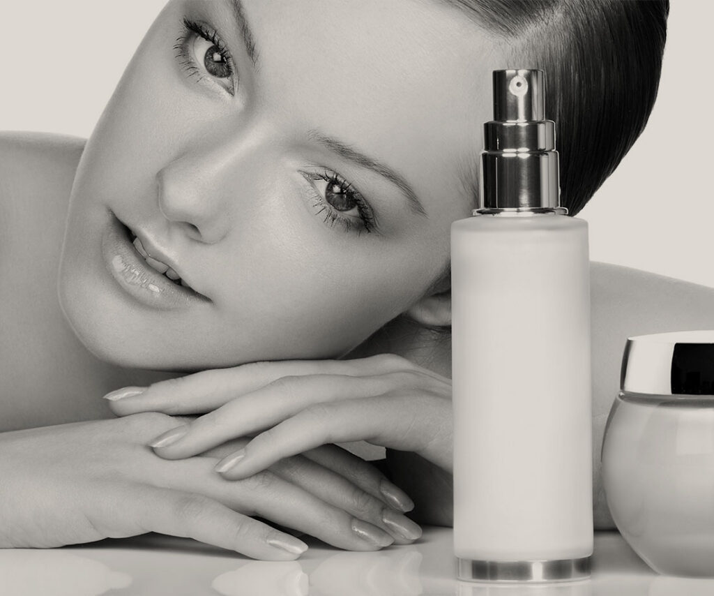 Woman resting her head on her hands beside a skincare spray bottle