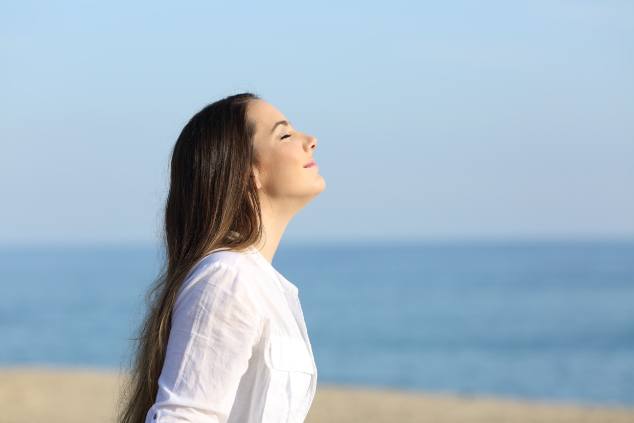 Woman breathing deeply outdoors with her face lifted toward the sunlight